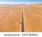 Small photo of Drone image of offroad vehicle driving on barren and dry desert road in Sossusvlei, Namibia, with high orange sand dunes