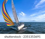 Small photo of Drone shot of the bow of a sailboat healed over with a bright colourful genoa, gennaker, or asymmetric spinnaker headsail in windy conditions under blue sky in The Netherlands