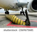 Yellow cooling airconditioning hose or pipe out of tarmac ground point with red lines connected to underside of airplane