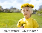 Small photo of Towheaded boy in wreath of flowers with bouquet of dandelions stand in meadow. Summer vacation time