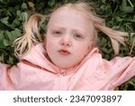 Small photo of Portrait of caucasian blonde girl with blue eyes lying on green grass . Towheaded little girl outside. Spring time.
