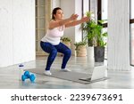 Small photo of Workout at home - middle aged woman performs squat exercise while looking into a laptop monitor. She uses an online tutorial.