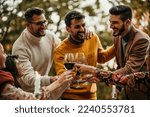 Small photo of Group of elegantly dressed friends having a small boho wedding outdoors in a garden, drinking wine, and talking to each other with a great mood and smiles.