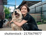 Dog at the shelter. Animal shelter volunteer takes care of dogs. Lonely dogs in cage with cheerful woman volunteer. 