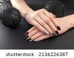 Black and silver manicure on black background. Close up of female hands with black nails. Nail art and design. Body care. Almond shaped type