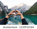 Love to travel and adventure. Woman hiker shows heart sign on background of Dolomites Mountaines. landscape of Braies Lake (Lago di Braies), hiking in alpine lake, Alps, Dolomites, Italy, Europe