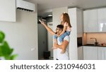 Small photo of Father with little daughter on shoulders turn on air conditioner using remote control. Happy family adjust comfortable temperature of cooler system