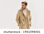 man in coat holds hands in pockets fashion modern style look aside light background
