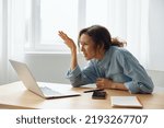 Small photo of What is happened. Confused unhappy beautiful curly woman office worker in perplexity raises hand up and looks furiously at broken laptop that gives out an error. Unexpected error on computer device