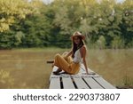 A hippie woman sits on a bridge by the river and enjoys the beautiful scenery around her