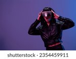 Small photo of Emotional awesome brunet woman in leather jacket touch trendy specular sunglasses both hands open mouth posing isolated in blue violet color light background. Neon party Cyberpunk concept. Copy space