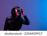 Small photo of Excited awesome brunet woman in leather jacket touch trendy specular sunglasses open mouth look aside posing isolated in blue violet color light background. Neon party Cyberpunk concept. Copy space