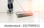 Small photo of Master with needle roller for new screed concrete with mixture of cement for leveling for floors with sunlight, building renovation banner.