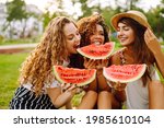 Cheerful happy friends camping on the grass, eating watermelon, laughing. Three young woman relaxing and enjoying holidays together. People, lifestyle, travel, nature and vacations concept.