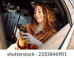 Smiling woman using smartphone while sitting in the back seat of a car. Young woman checks mail, texts, blogs in the car. Business, technology concept.