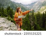 Wanderings. Stylish young woman traveler with a yellow backpack, holds a map, explores hiking trails in the mountains. The concept of travel, vacation.