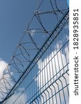 Small photo of High fence with barbed wire. Against the blue sky. The barrier is metal. Passage is forbidden. Restricted area. Protected area. Sharp iron spikes. Steel fence. Insurmountable barrier.