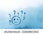 Small photo of joyless smile face with question marks around head painted on blue window flooded with raindrops on blur glass background in city