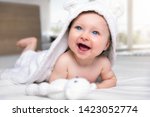 Portrait of a cute, laughing baby girl with a hooded towel on a white bed