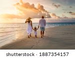 A elegant family in white summer clothing walks hand in hand down a tropical paradise beach during sunset tme and enjoys their vacation time
