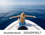 A blonde woman with outstretched arms sits on a boat over calm, blue sea and enjoys her freedom