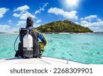 Small photo of A scuba diver in his diving gear sits in front of a boat and enjoys the view of the tropical landscape with turquoise sea in Krabi, Thailand