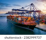 A large container cargo ship is beeing loaded in a commercial dock during sunset
