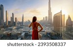 Small photo of A beautiful luxury woman in a red dress enjoys the sunset view behind the modern skyline of Dubai city, UAE