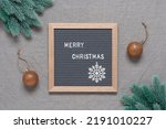 Merry Christmas lettering on letter board. Gray felt board in a wooden frame with text. Beautiful xmas background with fir branches, golden balls. Gray textile background. Top view, flat lay.