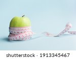 Apple with measuring tape on blue background. Weight loss, counting calories and healthy eating concept - calculate daily nutrition intake. Copy space.