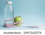 Bottle of water, apple with measuring tape on blue background. Weight loss, counting calories and healthy eating concept - calculate daily nutrition intake. Copy space.