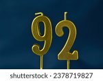 Small photo of close up on gold number ninety-second birthday candle on a dark background.