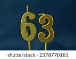 Small photo of close up on the gold number sixty-third candle on a dark background.