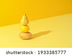 Minimal concept with potato, lemon, and a pear stacked on a yellow background in bright light. Yellow monotone image with vegetables and fruits.