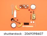 Food knolling on orange background with crepes ingredients and kitchen utensils. Making crepes flat lay, kitchen tools, and ingredients arranged with copy space in the middle.