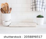 Small photo of Stylish white kitchen background with kitchen utensils and green houseplant standing on white countertop, copy space for text, front view