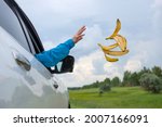A woman's hand throws banana peels out of the car window.