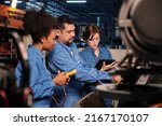 Small photo of Multiracial professional industry engineer teams in safety uniforms work by inspecting machines' voltage current, checking, and maintaining at manufacture factory, electric system service occupations.
