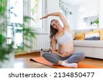 Portrait of young pregnant female working out at home. pregnant woman practicing yoga at home. Prenatal groins stretch. Buddha Konasana Pose. Pregnancy yoga and fitness.