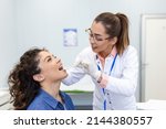 Small photo of Doctor using inspection spatula to examine patient throat. ENT doctor doing throat exam of a woman. patient opened her mouth to throat check-up