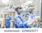 Small photo of Anesthetist Working In Operating Theatre Wearing Protecive Gear checking monitors while sedating patient before surgical procedure in hospital
