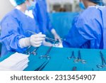 Small photo of Nurse hand taking surgical instrument for group of surgeons at background operating patient in surgical theatre. Steel medical instruments ready to be used. Surgery and emergency concept