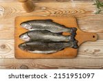 Raw trout on wood plate. Fresh cutthroat, three steelhead fish, whole rainbow trout, trutta, fario, Oncorhynchus mykiss, freshwater trouts on wooden background top view
