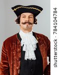 Small photo of mustachioed eccentric man in the vintage clothes of the baron. Hat tricorn, brown jacket. Funny pigtail hair. man dressed as a courtier