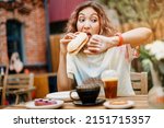 A girl in a hurry bites a burger on the run in a fast food cafe and looks at the smart watch. Late for a meeting and punctuality and digestive problems