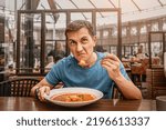 Small photo of dissatisfied unhappy customer of the restaurant sniffs the disgusting smell of a bowl of soup with spoiled ingredients and is going to complain to the chef