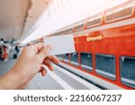 Small photo of Credit or prepaid transport card in the passenger's hand against the background of a modern double-decker high-speed train on the platform of the railway station