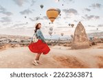 Small photo of Young girl in a red dress stood in awe as she watched vivid air balloons ascend into the sky in Cappadocia.