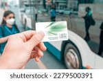 Small photo of 14 January 2023, Abu Dhabi, UAE: Hafilat prepaid transport card in the passenger's hand against the background of a modern city bus at city street