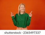 Beautiful young woman raising index fingers in eureka gesture on orange background